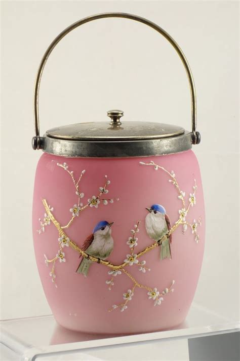 A Pink Vase With Two Birds Painted On The Front And Side Sitting On A Shelf