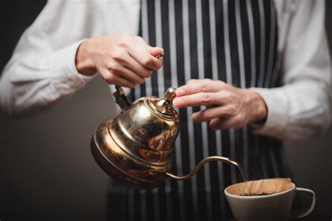 Barista despejando água quente da chaleira sobre o pó de café para