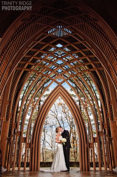 A Bride And Groom Standing In Front Of An Arched Wooden Structure At