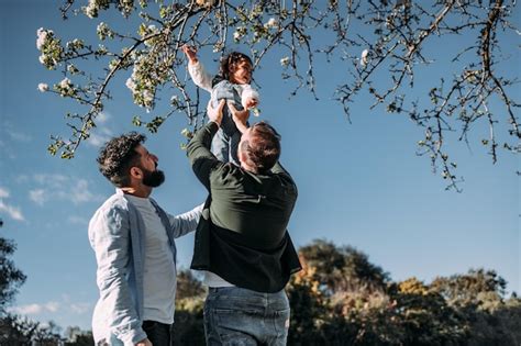 Pareja gay masculina levantando a su joven hija para tocar las flores de un árbol concepto de