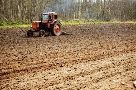 An Agricultural Tractor Plows The Land In A Field In The Spring Stock