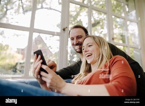 Laughing Couple Using Smartphone At Home Stock Photo Alamy