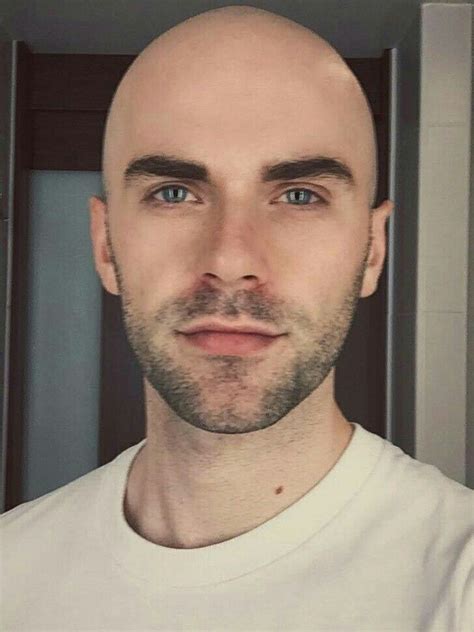 A Bald Man With Blue Eyes And A White T Shirt Looks At The Camera