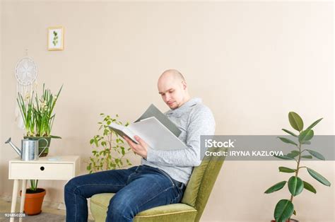 Portrait Of Bald Man Reading Big Book While Sitting In Armchair Young