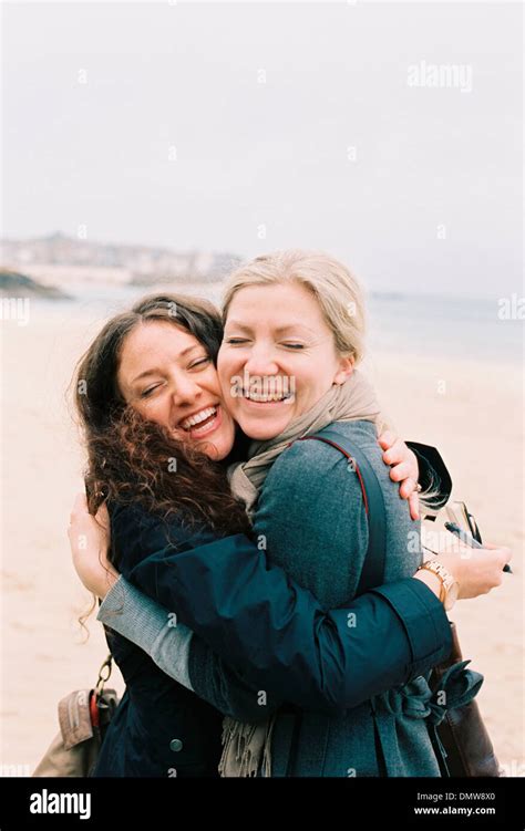 Two women cheek to cheek hugging on a beach Stock Photo - Alamy