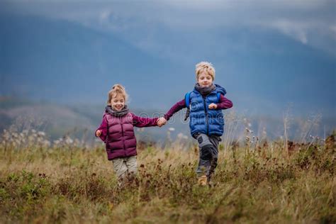 Little Children Holding Each Other Hands And Runing At Autumn Meadow