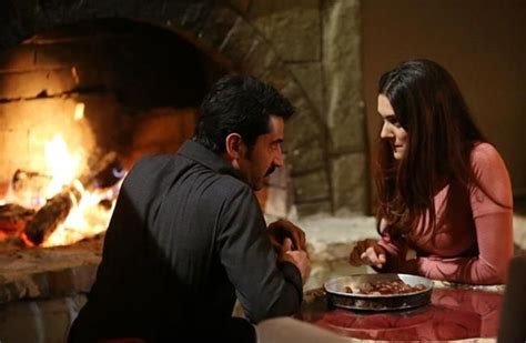 A Man And Woman Sitting At A Table In Front Of A Fire Place Eating Pizza