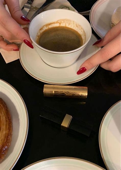 Two Hands Holding A Cup Of Coffee On Top Of A Table With Other Plates