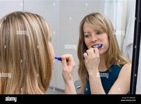 A Young Woman Brushing Her Teeth In Front Of A Bathroom Mirror Stock