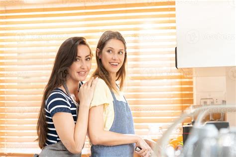 Lesbian Couple Standing In Kitchen Lesbian Couple Standing In A Modern Kitchen Behind A Counter