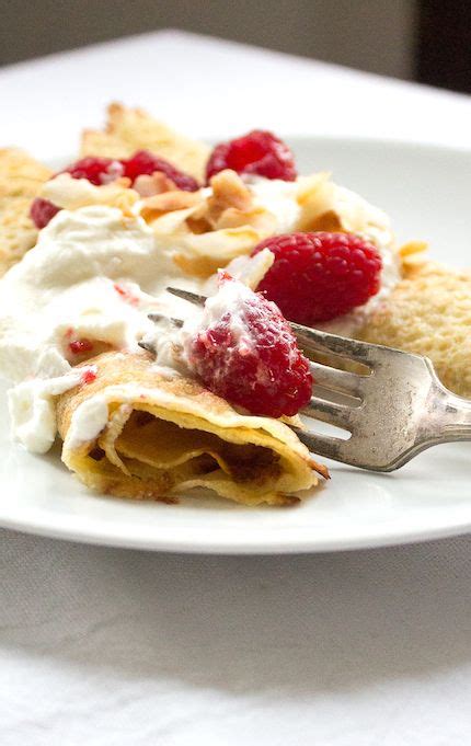 A White Plate Topped With Crepes Covered In Whipped Cream And Raspberries