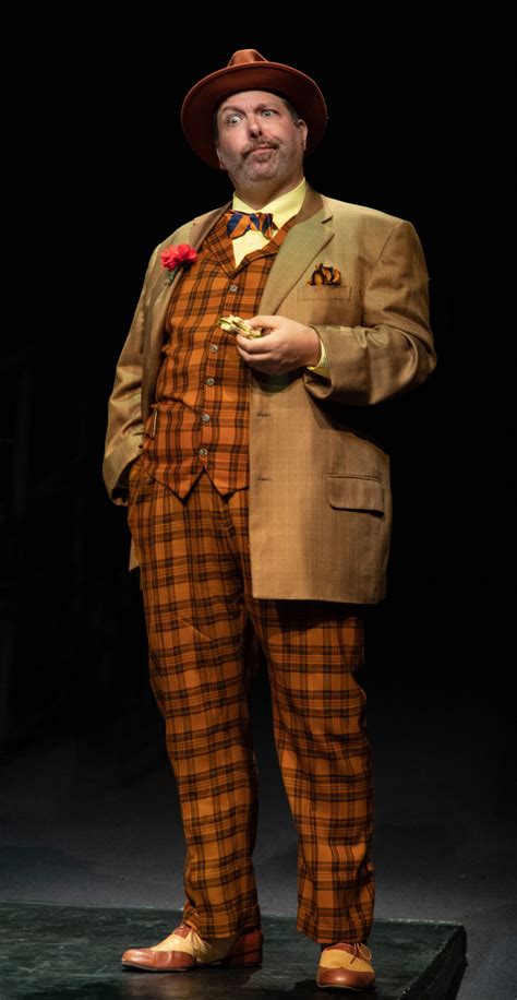 A Man In A Suit And Tie Standing On A Stage With His Hands In His Pockets