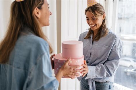 Excitée jeune femme caucasienne blonde recevant un cadeau de son amie à l intérieur Concept de