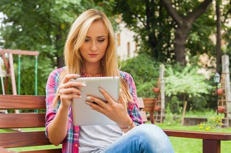 Sensual Blonde Woman Sitting In Park On Wooden Bench She Is Using