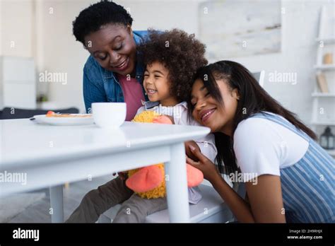 Happy African American Women Hugging Cheerful Girl During Breakfast