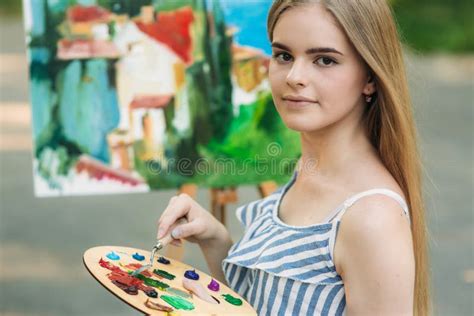 La Muchacha Del Blonde Pinta Una Pintura En La Lona Con La Ayuda De Las Pinturas Un Caballete De