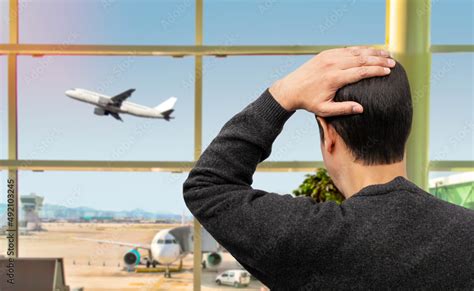 Rear View Of A Sad Man Looking At A Plane Taking Off And Missing His Flight At Airport Stock