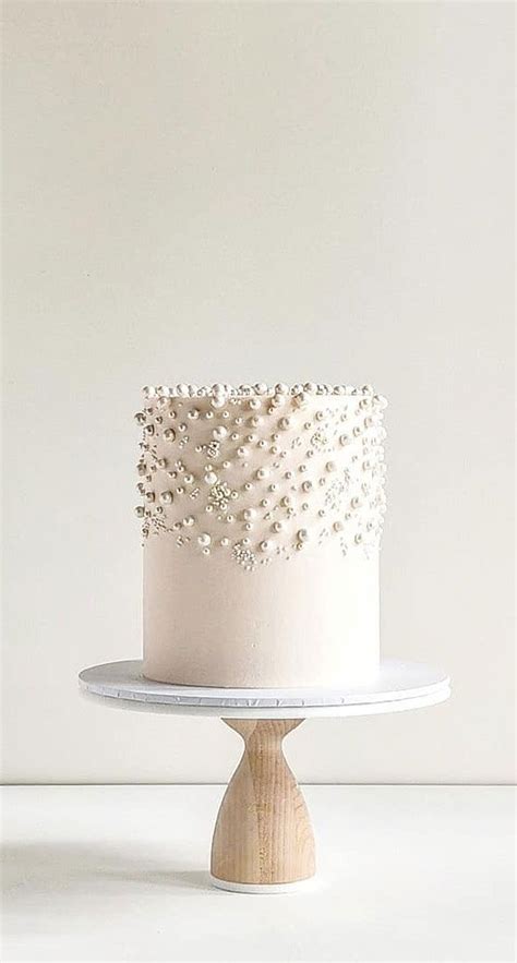 A White Cake With Pearls On Top Sitting On A Wooden Stand In Front Of A