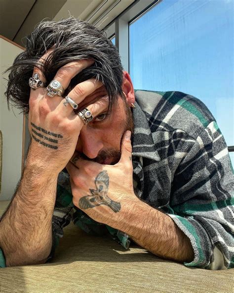 a man with tattoos on his arms and hands resting his head against his ...