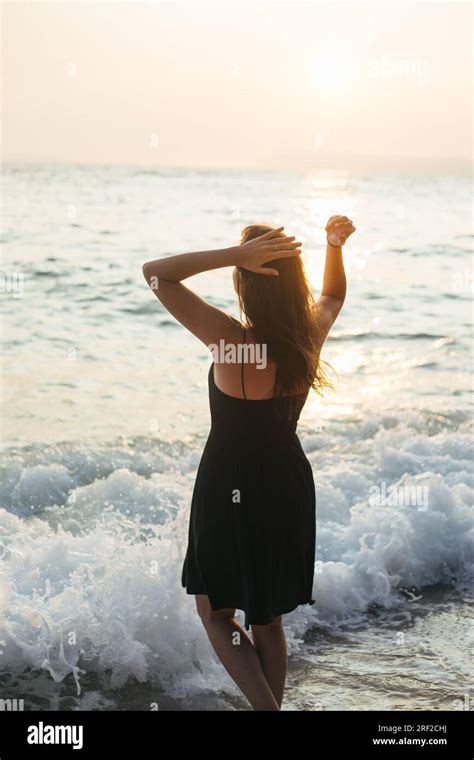 Back View Of Woman Standing In Sea Shallows During Sunset Stock Photo