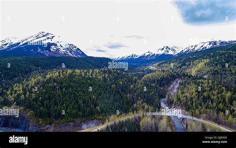 An Aerial View Of Snowy Mountains Covered With Forests On A Cloudy Sky