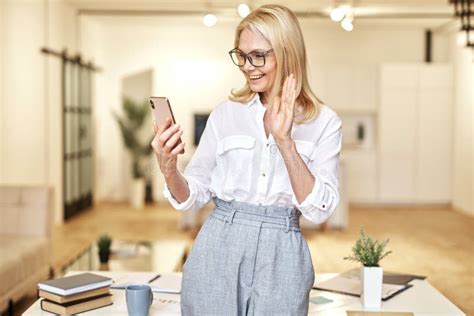 Happy Mature Businesswoman Waving At Camera Having Online Video Call Using Smartphone While