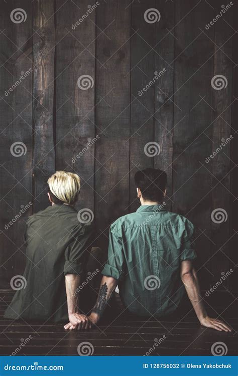 Pares Gay Jovenes Que Se Sientan En El Piso Delante De La Pared De Madera Foto De Archivo
