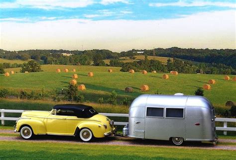 An Old Yellow Car Pulling A Trailer With Hay Bales In The Background On