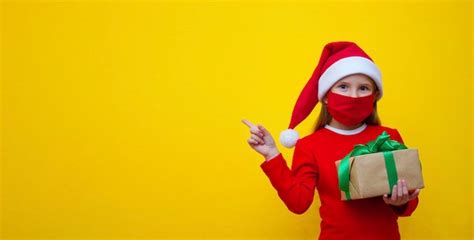 Menina máscara médica de chapéu de papai noel segurando um presente