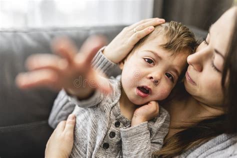 Devoted Mother Hugging And Comforting Her Son On Sofa Stock Photo