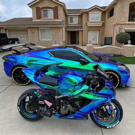 A Blue And Green Motorcycle Parked In Front Of A House With Two Cars