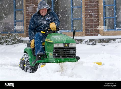 John Deere riding lawn mower fitted with a snow plow removing snow from a parking lot in Boise ...