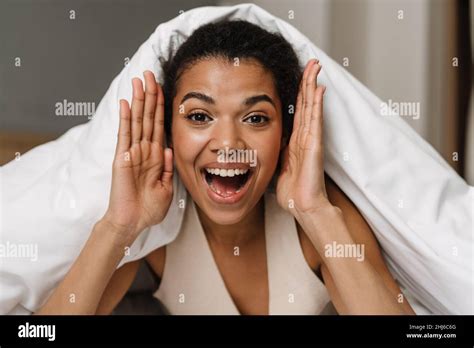 Happy Young African Woman Laying Hiding Under A Blanket On A Bed At