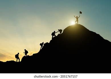 Silhouette Hikers Helping Each Other Climb Stock Photo