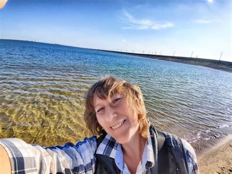 Blonde Woman Enjoys A Coastal Excursion While Taking A Selfie Near The Sparkling Water On A