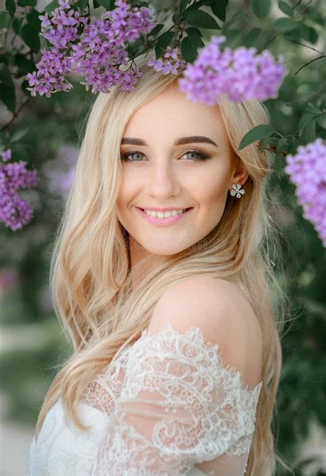 Blonde Bride With Naked Shoulders Stands Under Green Branches Stock