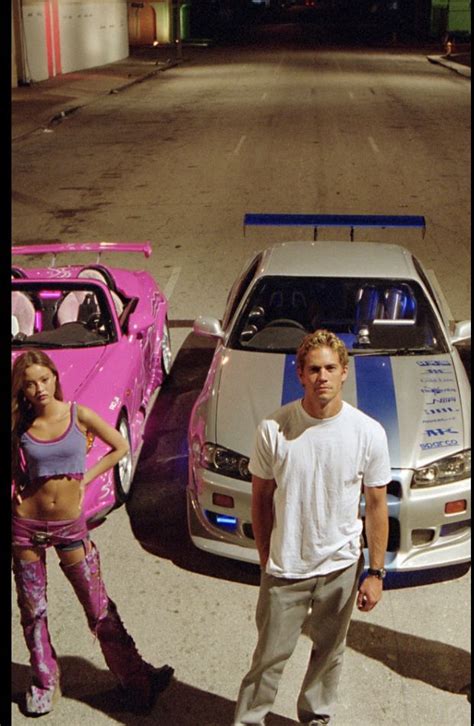 A Man Standing Next To A Woman In Front Of Two Cars