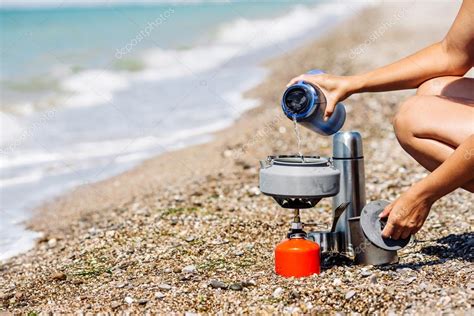 Woman Boiling Water On Camping Stove On Sea Shore Bushcraft Equipment