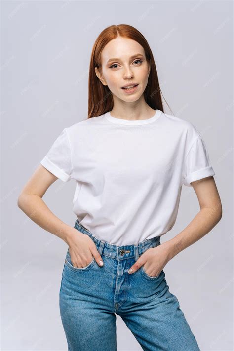 孤立した白い背景に舌を示すtシャツとデニムパンツを着てうれしそうな若い女性スタジオコピースペースで感情的に表情を示す赤い髪のきれいな女性モデル