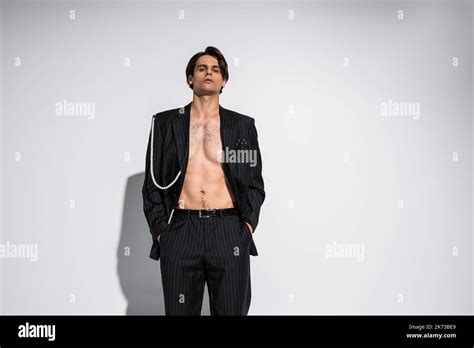 Brunette Model In Trendy Suit With Pearls Posing With Hands In Pockets On Grey Background Stock
