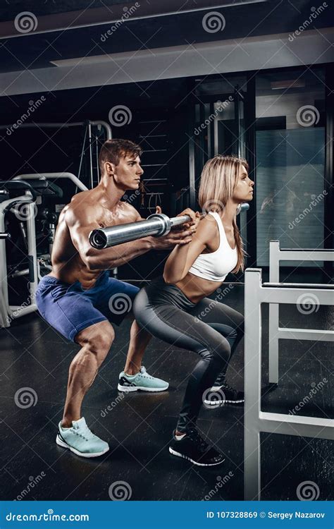 Personal Trainer Helping A Young Woman Lift A Barbell While Working Out