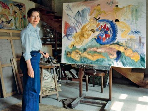 A Woman Standing In Front Of An Easel With Paintings On It