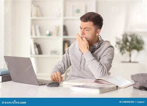 Hombre Sentado Frente A Una Laptop En Casa Y Bostezando Foto De Archivo