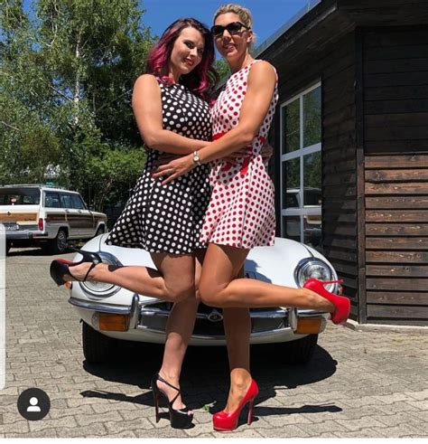 Two Women Hugging Each Other In Front Of A White Car With Red Heels On It