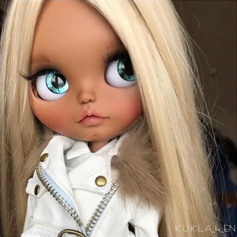 A Doll With Long Blonde Hair And Blue Eyes Wearing A White Coat Fur Collar