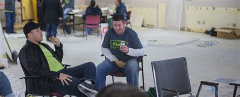 Two Men Sitting In Chairs Talking To Each Other While Others Stand And