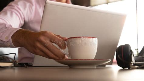 Man S Hand Picking Up A Cup Of Coffee Behind The Laptop Stock Photo