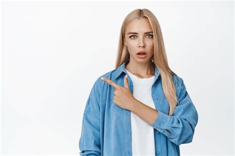 Fille blonde surprise pointant le doigt vers le coin supérieur gauche haletant d admiration l