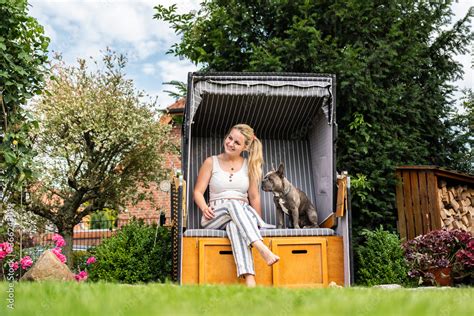 Junge Blonde Frau Sitzt Mit Ihrem Hund Im Eigenen Strandkorb Im Garten Foto De Stock Adobe Stock