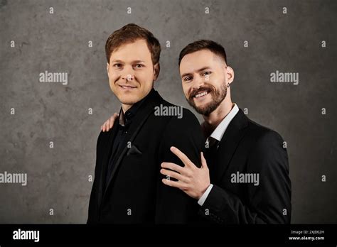 A Loving Gay Couple Poses In Elegant Suits Against A Gray Backdrop Stock Photo Alamy